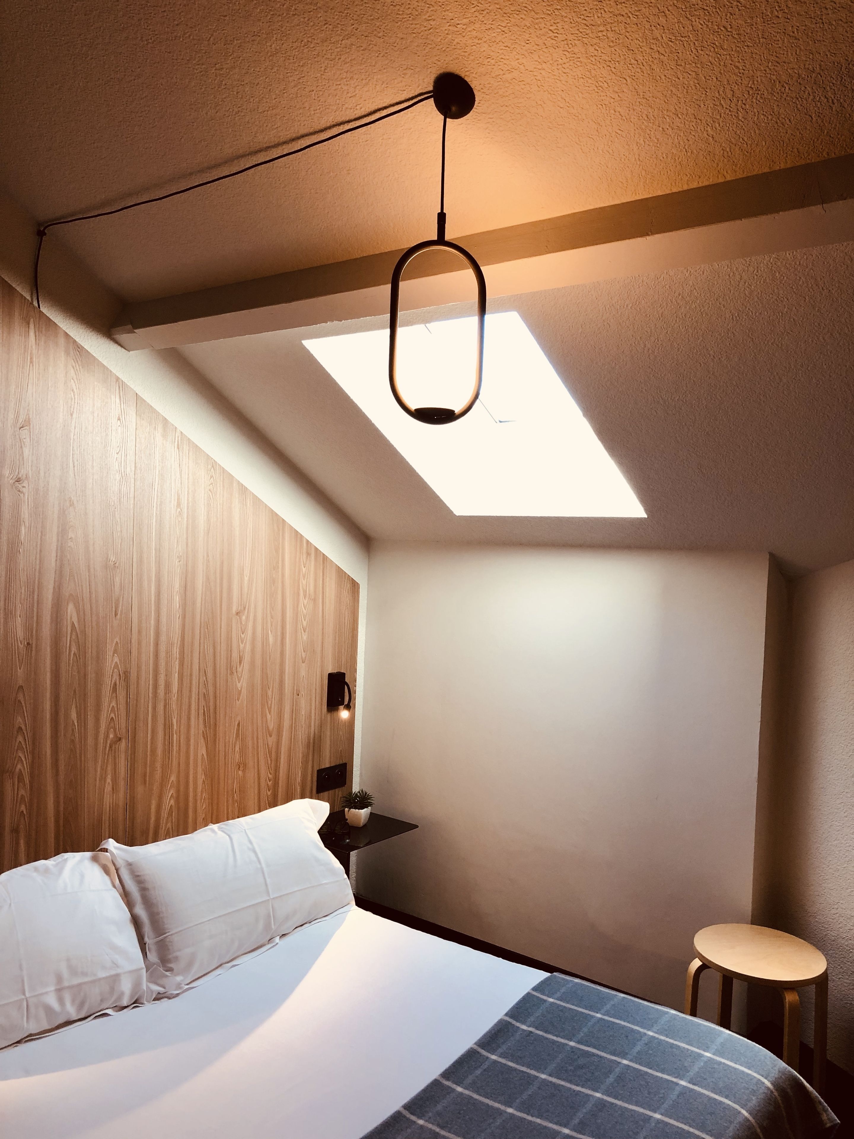 Een moderne slaapkamer met dakraam, een bed, nachtkastje en een klein krukje.