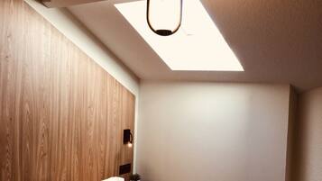 A modern bedroom with a skylight, a bed, a bedside table, and a small stool.