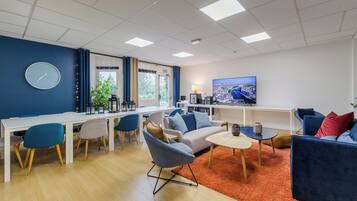 A modern living room with a dining area, a sofa set, a TV, and a clock on the wall.