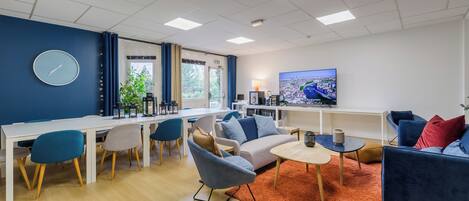 Una sala de estar moderna con comedor, un conjunto de sofás, un televisor y un reloj en la pared.