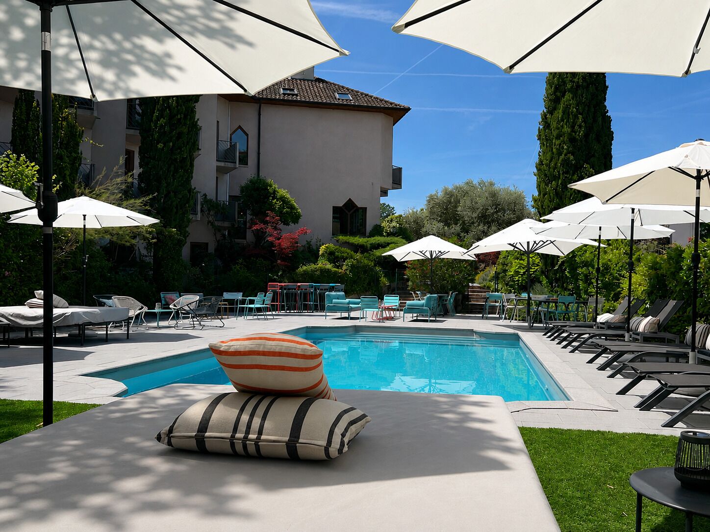 Un espace piscine avec des chaises longues, des parasols et un bâtiment en arrière-plan.