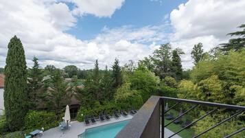 Un espace piscine agrémenté de chaises longues et de parasols, entouré d’une végétation luxuriante et d’arbres.