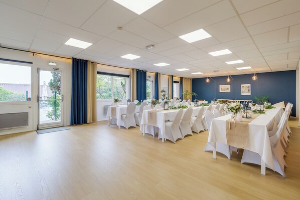 A conference room with multiple tables, white chairs, and a view of the outdoors through large windows. - Best Western Bridge Hotel Lyon East (Jons)