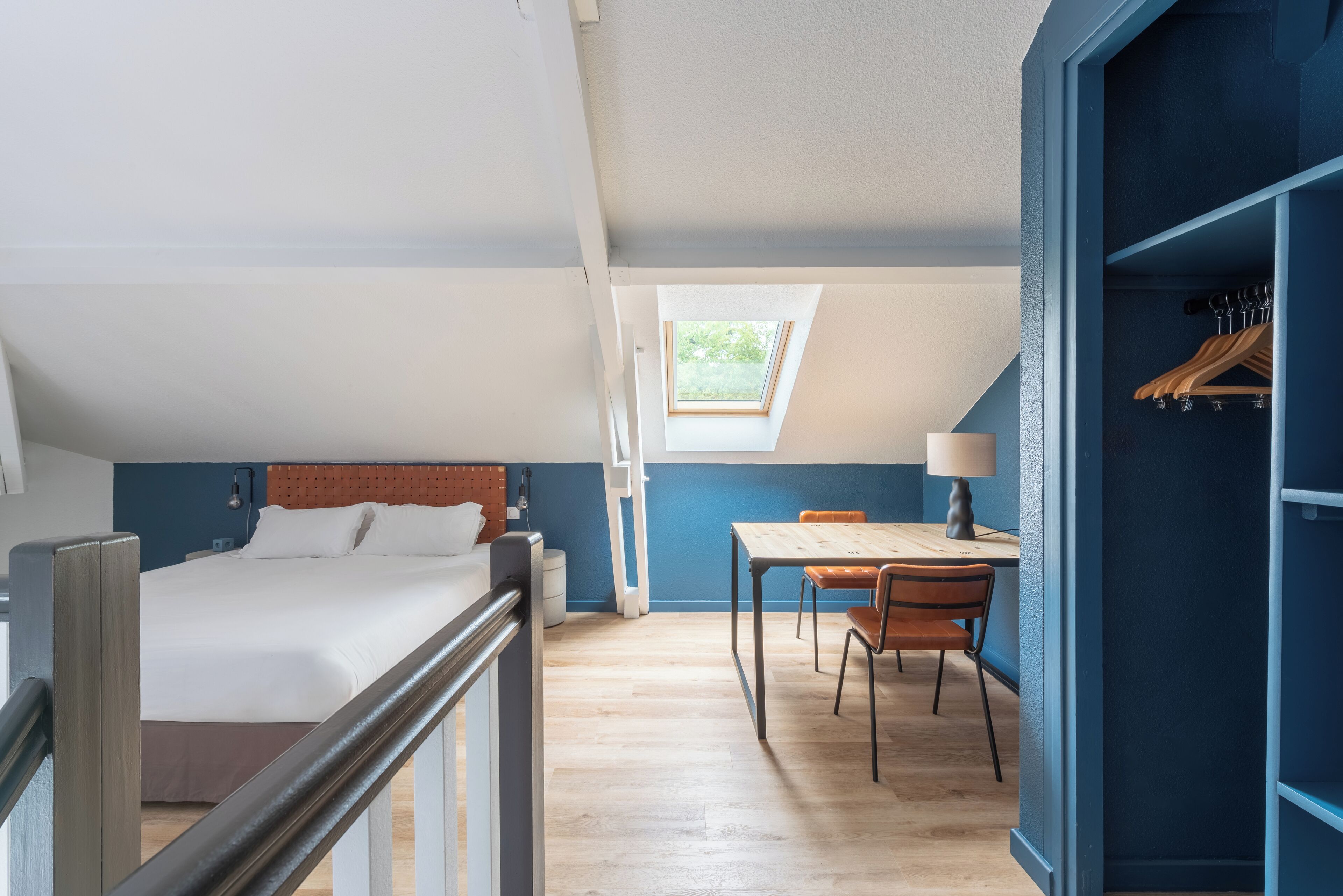 A bedroom with a bed, a desk, and a chair. There is a skylight above the desk.