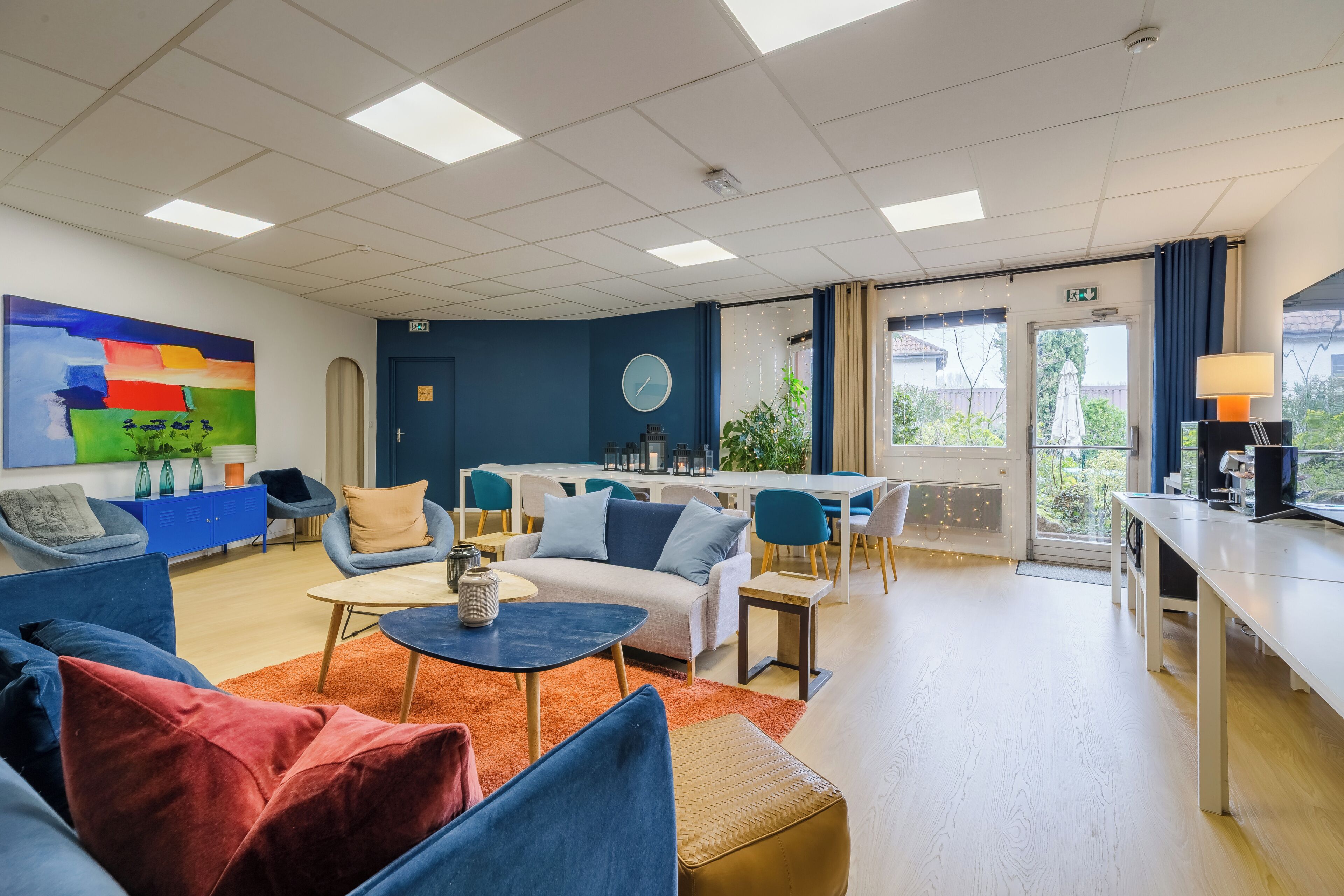 Een moderne hotel lobby met blauwe banken, een salontafel, een eetgedeelte en een groot schilderij aan de muur.