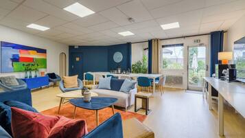 Een moderne hotel lobby met blauwe banken, een salontafel, een eetgedeelte en een groot schilderij aan de muur.