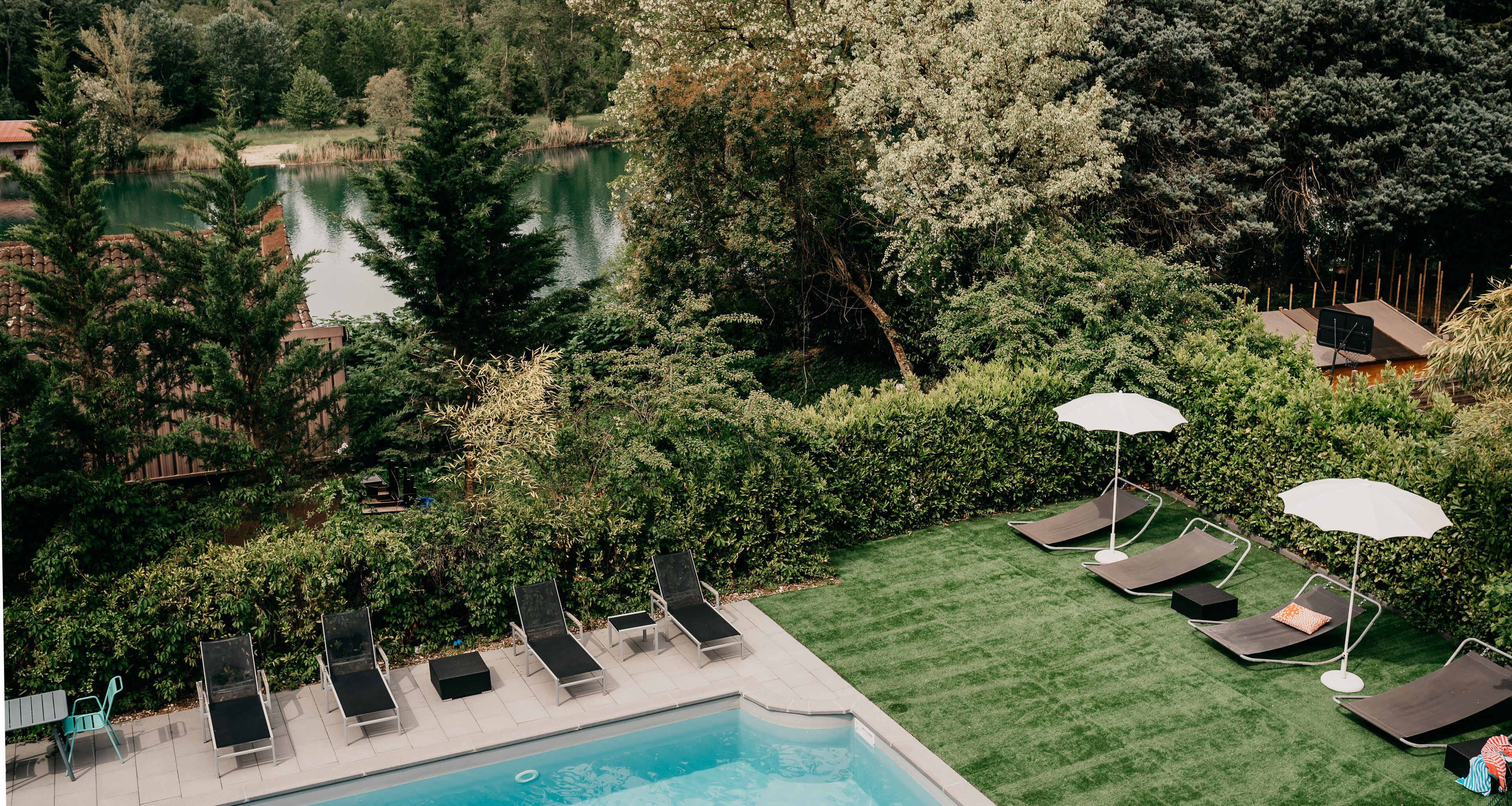 Une piscine entourée de verdure, avec des chaises longues et des parasols, et offrant une vue sur un lac.