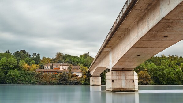 A concrete bridge over a calm river with a house in the background.