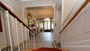 A grand staircase with a red carpet, white walls, and a chandelier.