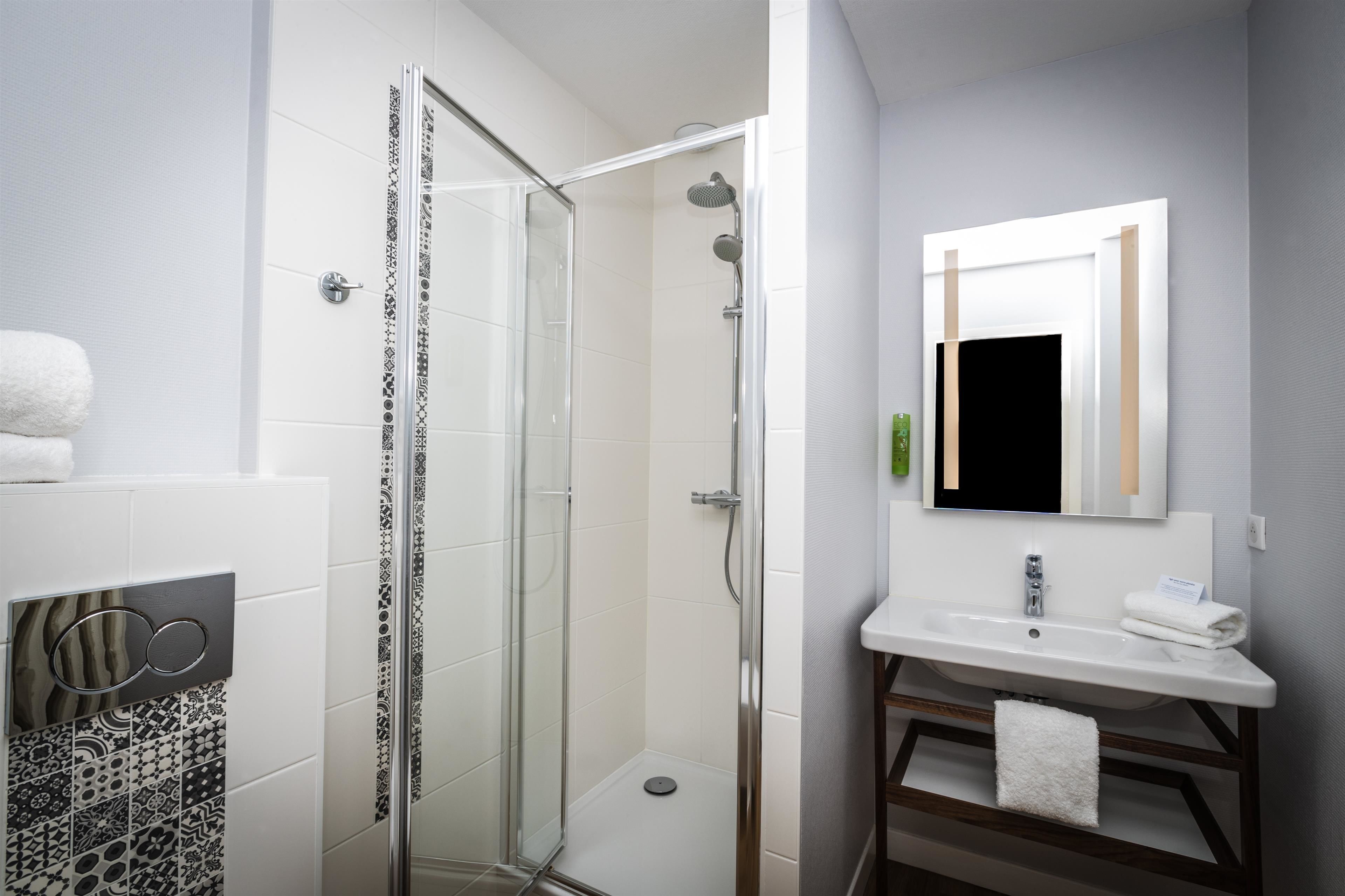 A modern bathroom with a glass-enclosed shower, a white sink, and a mirror above it.