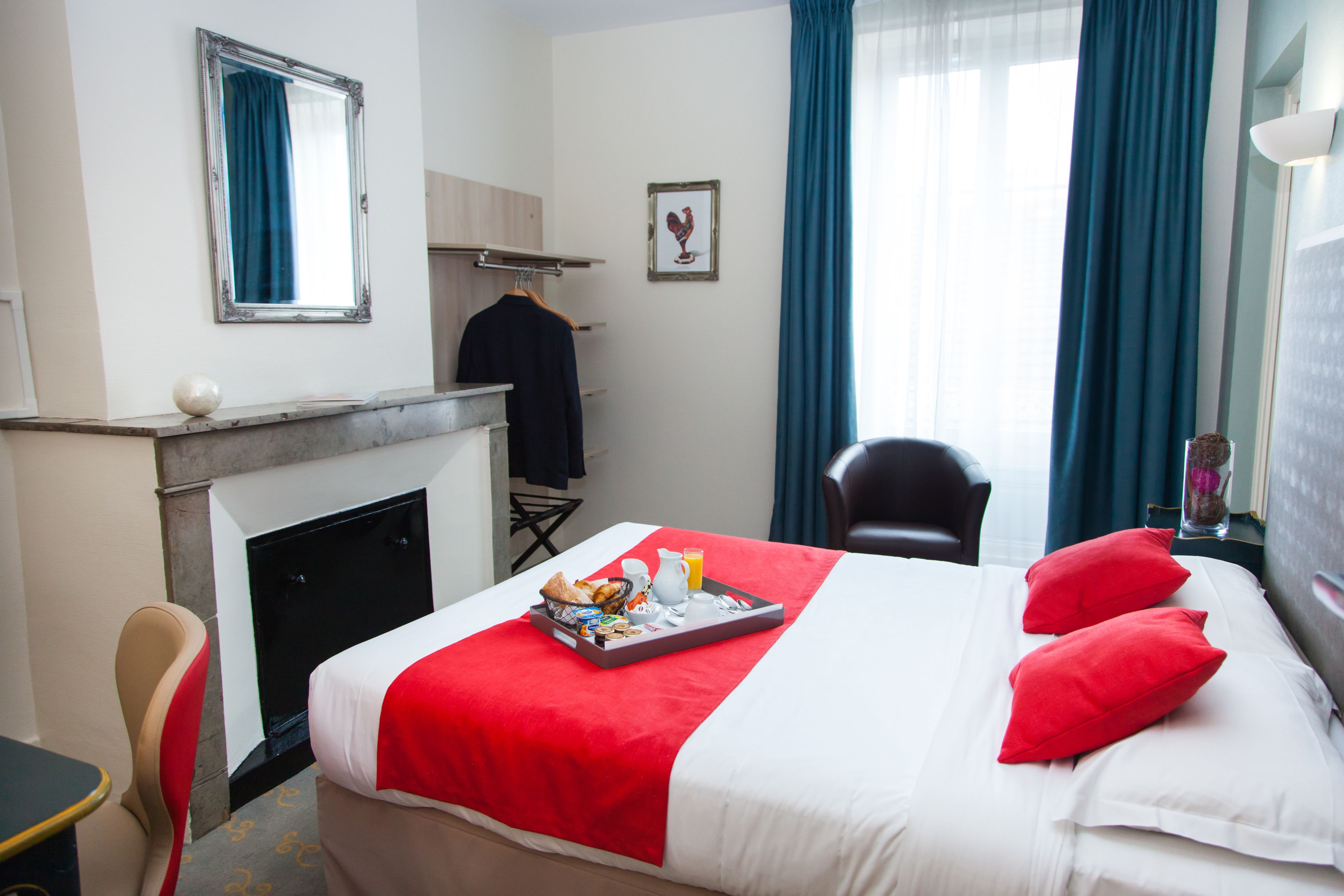 Habitación de hotel con cama, una silla, una mesita, chimenea y ventana con cortinas.