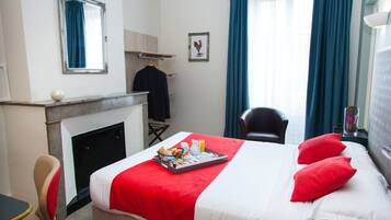 Ein Hotelzimmer mit Bett, Sessel, kleinem Tisch, Kamin und einem Fenster mit Vorhängen.