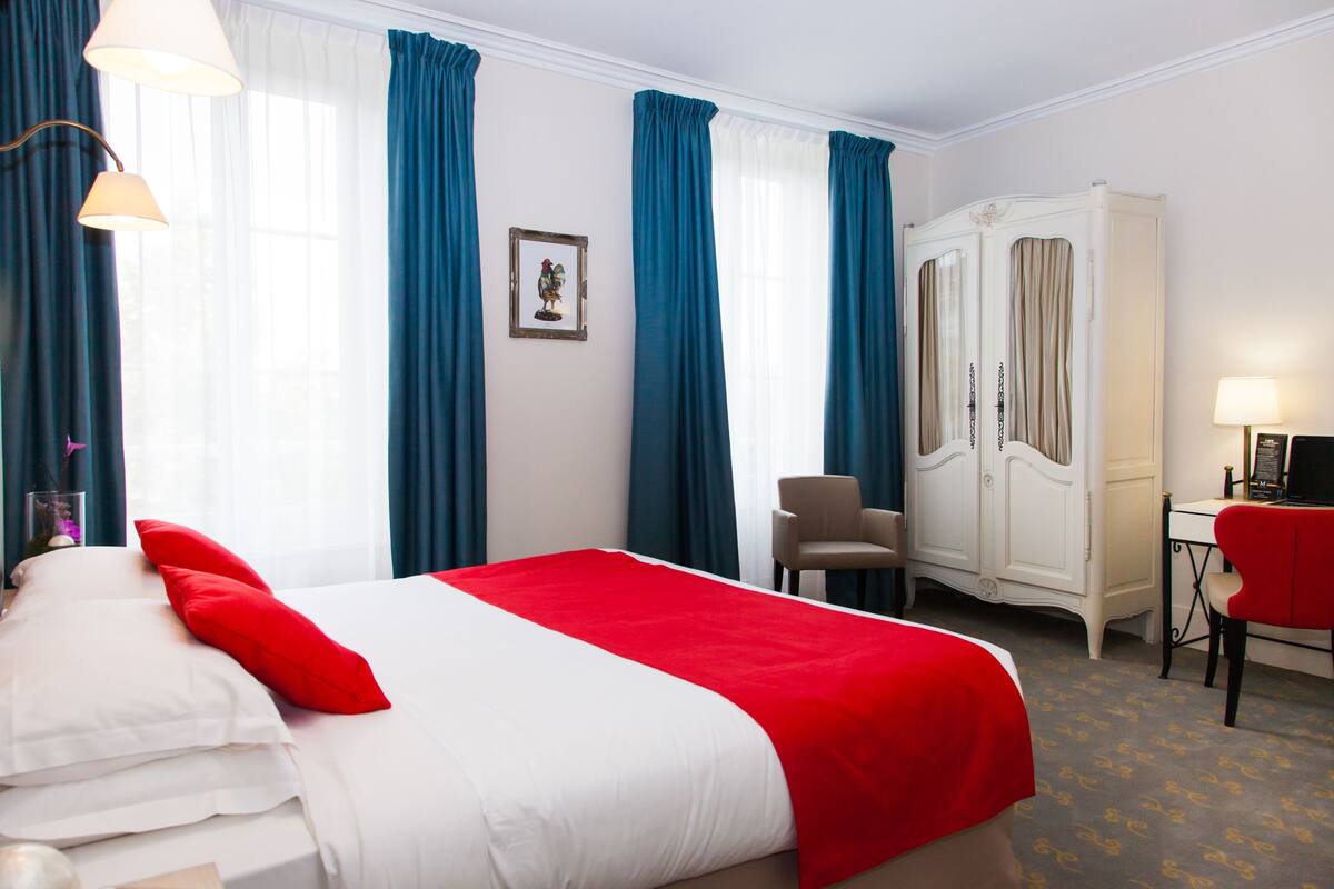 A hotel room with a bed, a desk, a chair, and a wardrobe.
