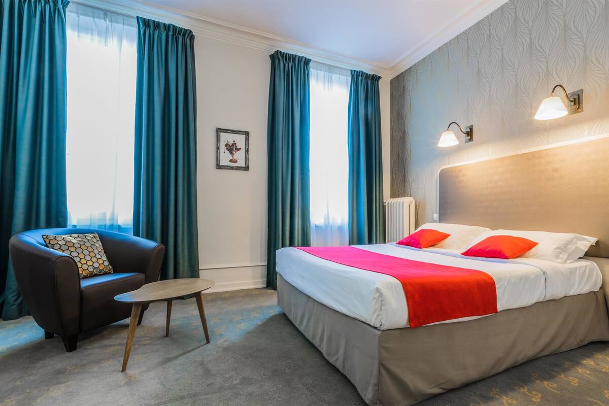 Ein Hotelzimmer mit Bett, Stuhl, kleinem Tisch und einem Bild an der Wand.