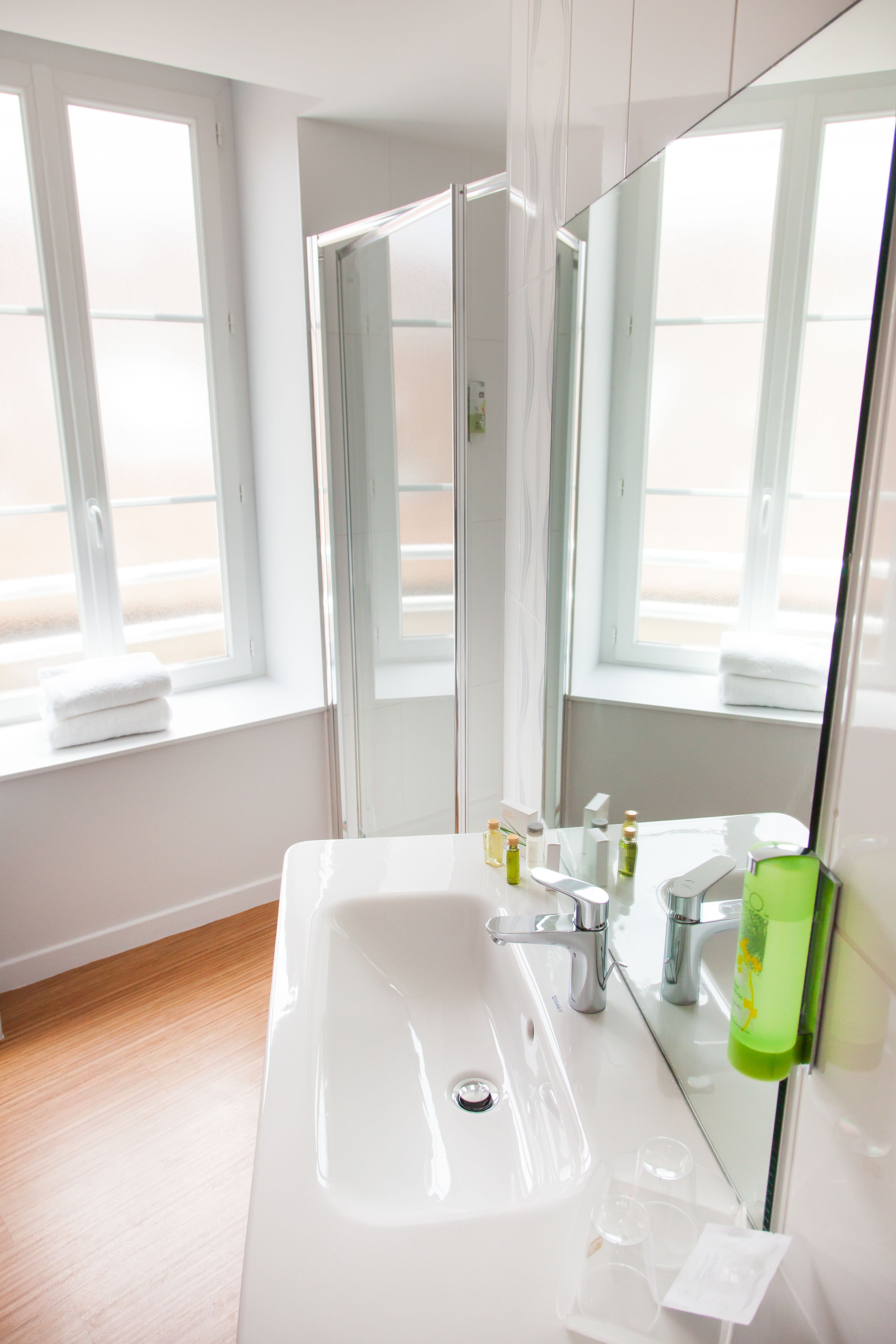 A modern bathroom with a large white sink, a mirror, and a window with a towel on the sill.