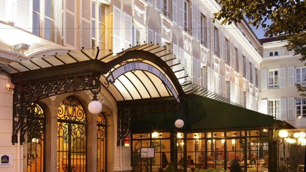 A hotel entrance with a covered patio area, ornate ironwork, and a sign reading "HOTEL DE FRANCE".