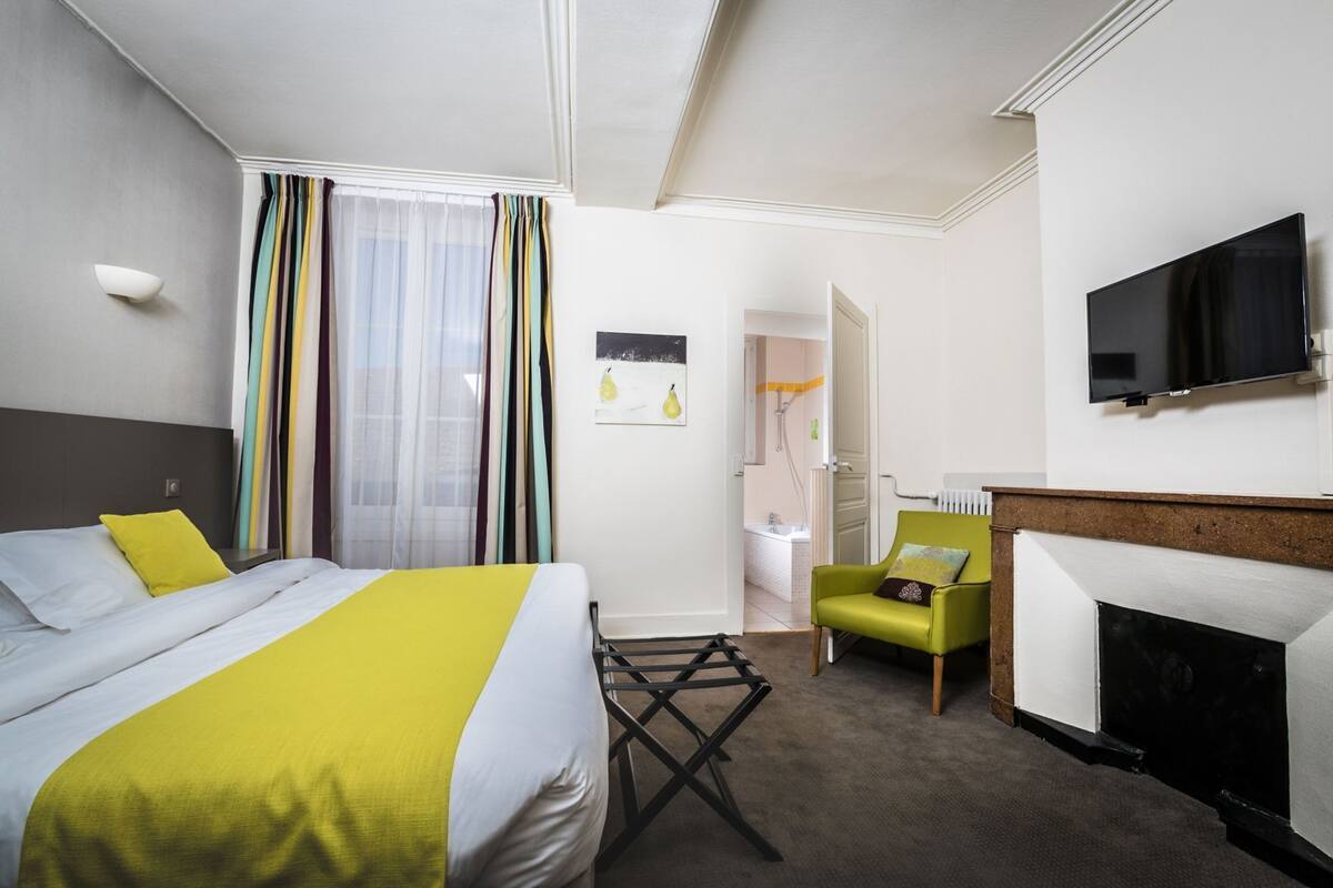 A hotel room with a bed, a chair, a television, and a fireplace.