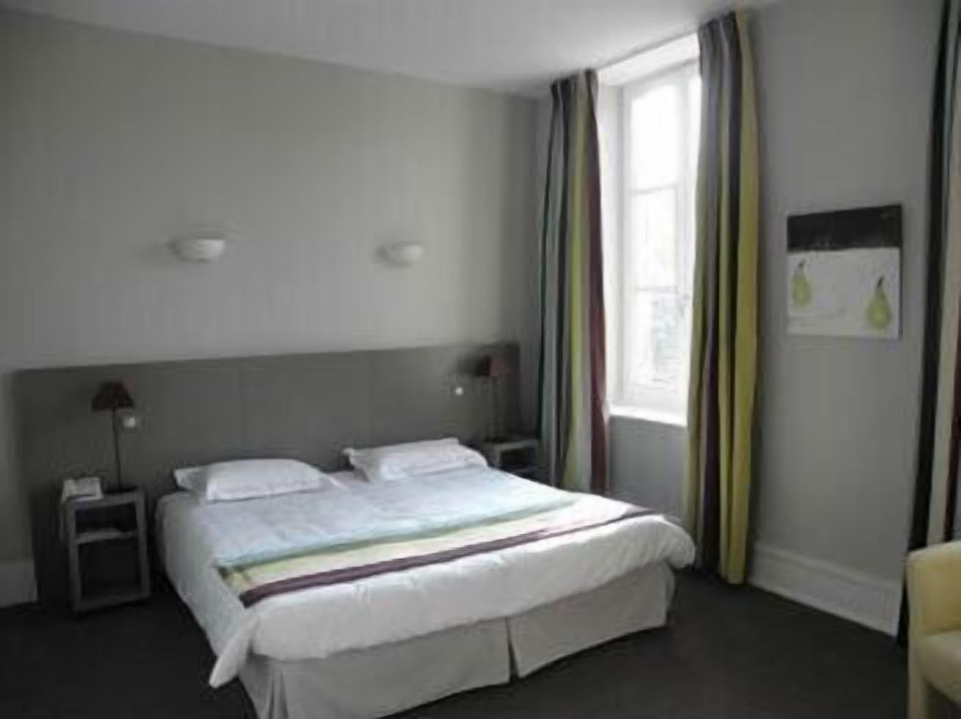 A hotel room with a bed, nightstands, a lamp, a window with curtains, and a wall-mounted light fixture.