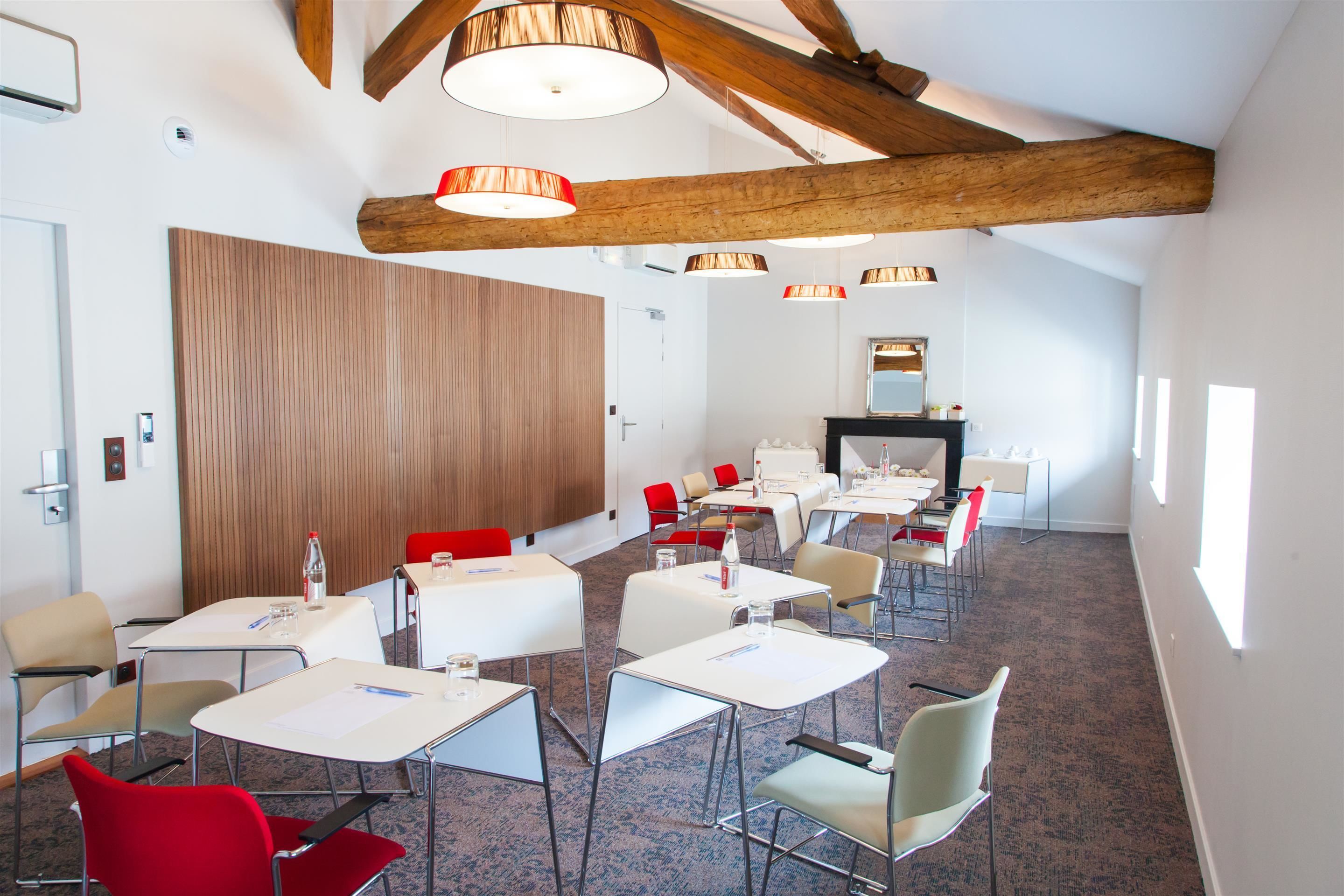 A conference room with white tables, red and beige chairs, wooden beams, and pendant lighting.