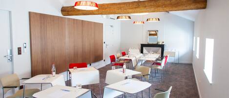 A conference room with white tables, red and beige chairs, wooden beams, and pendant lighting.