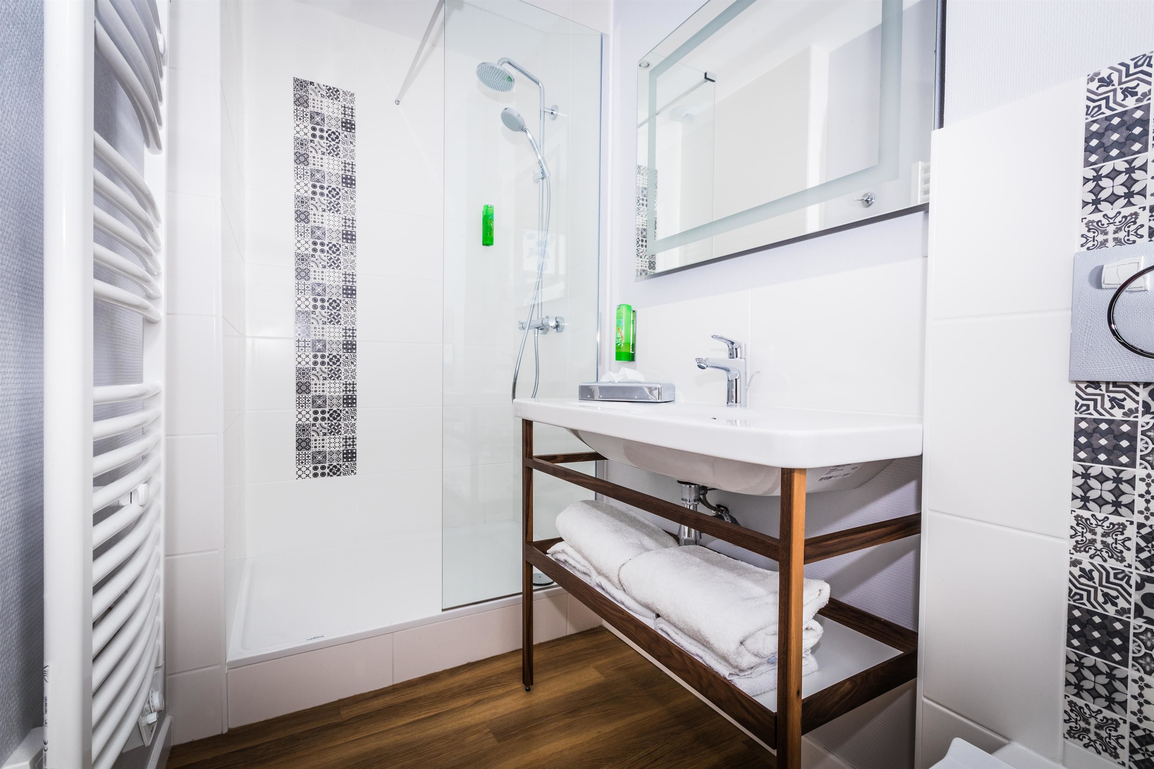 A modern bathroom with a glass shower enclosure, a white sink with a mirror above it, and patterned tiles on the walls.