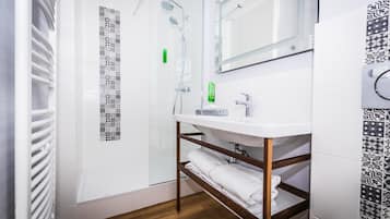 A modern bathroom with a glass shower enclosure, a white sink with a mirror above it, and patterned tiles on the walls.