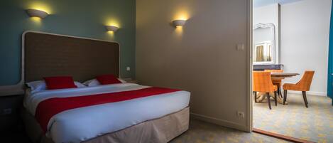 A hotel room with a bed, two wall-mounted lights, a dining area with a table and chairs, and a mirror.