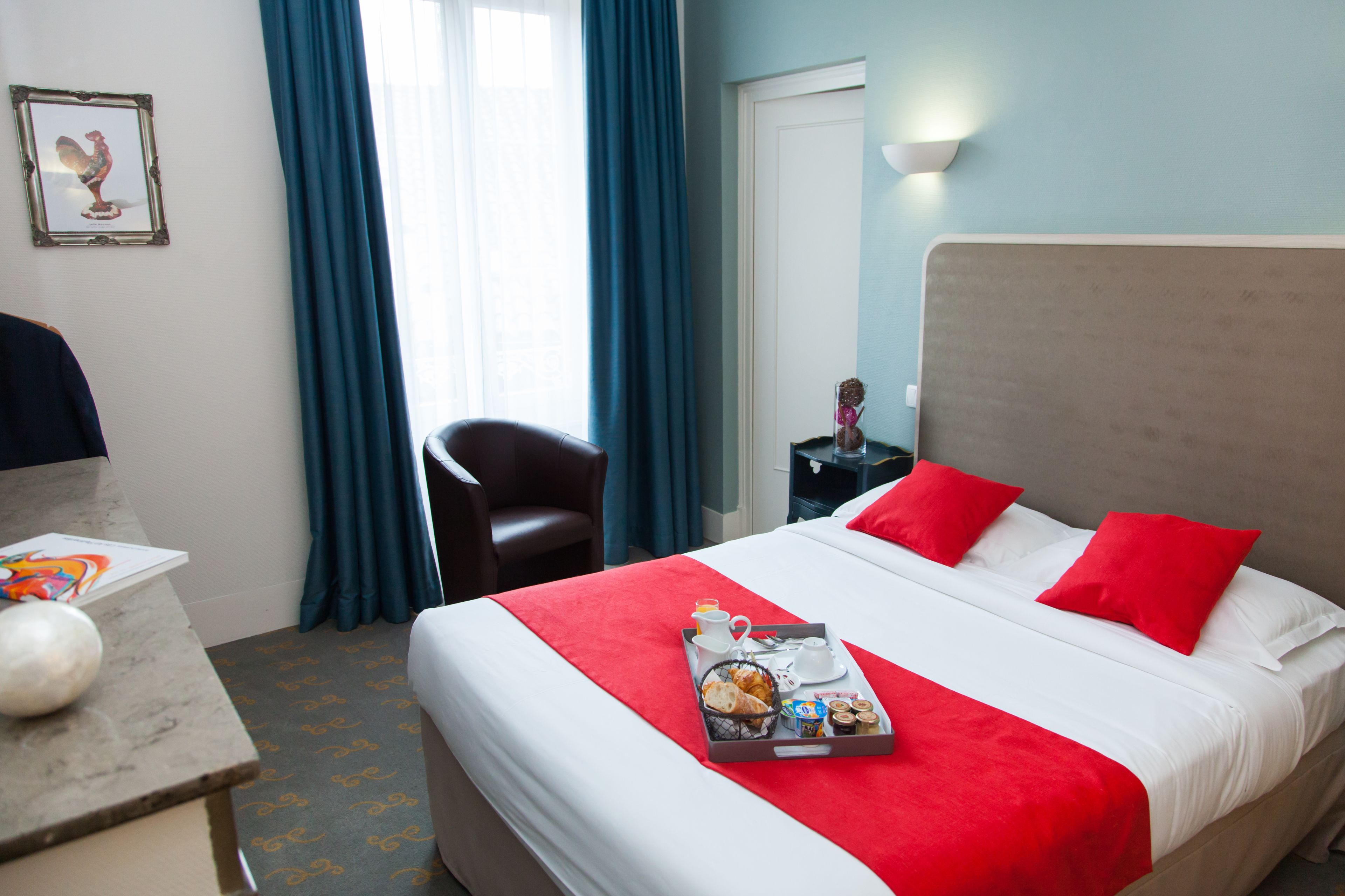 A hotel room with a bed, a desk, a chair, a tray with breakfast items, and a framed picture on the wall.