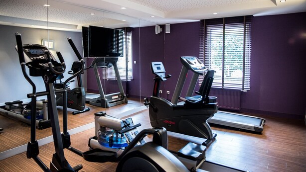 Un gimnasio moderno con máquinas de cardio, un espejo grande y amplias ventanas.