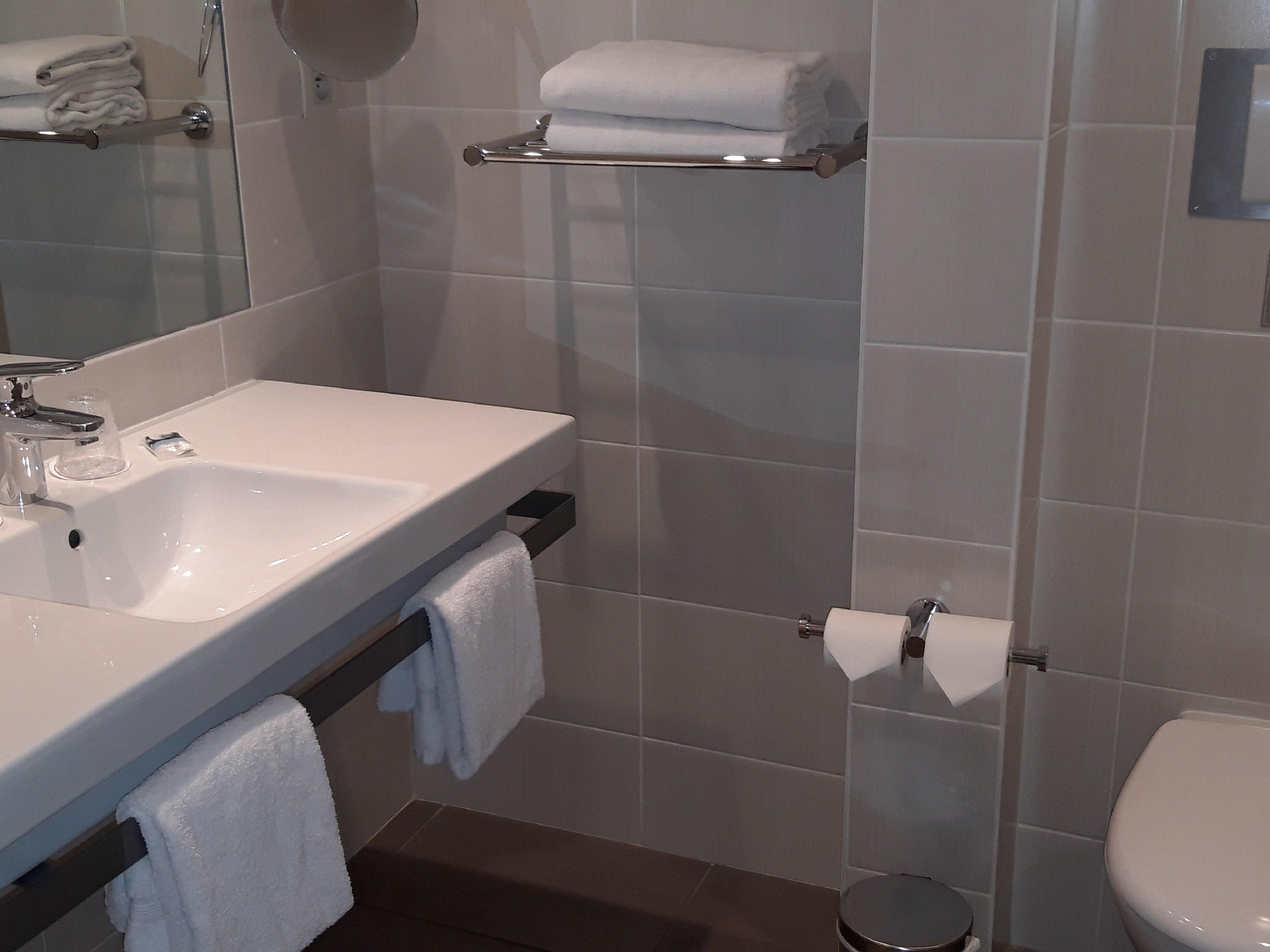 A bathroom with a sink, mirror, towel rack, toilet, and a small trash bin.