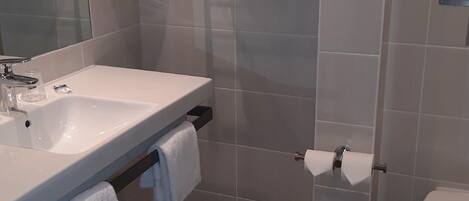 A bathroom with a sink, mirror, towel rack, toilet, and a small trash bin.