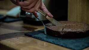 Una mano cortando un pastel redondo con un cuchillo sobre una tabla de madera.