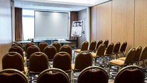 Une salle de conférence avec des rangées de chaises, un écran de projection et un tableau de présentation.