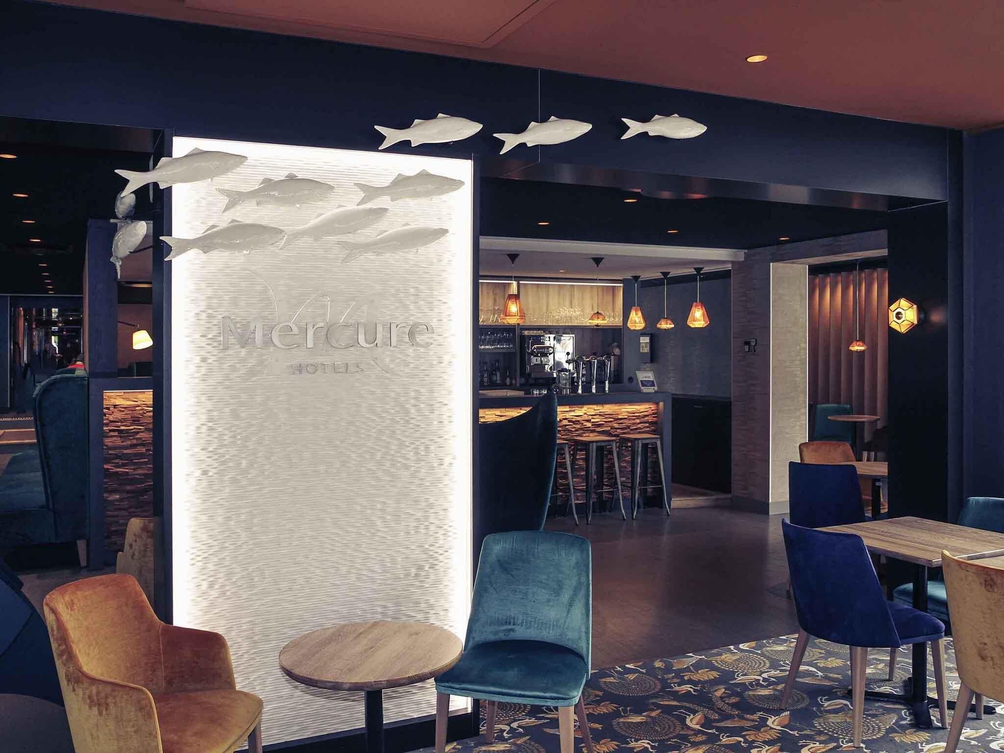 A modern interior with a bar area, seating with blue and wooden chairs, and a decorative wall with fish motifs.