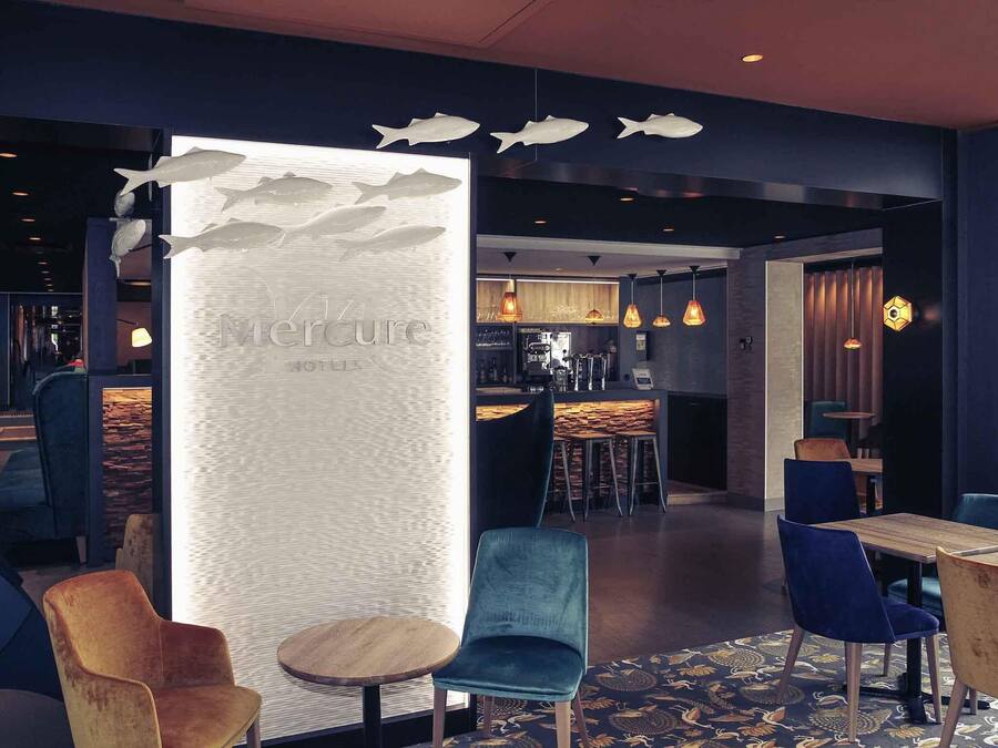 A modern interior with a bar area, seating with blue and wooden chairs, and a decorative wall with fish motifs.