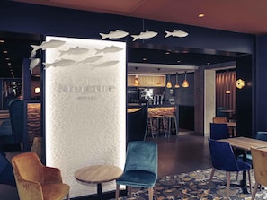 Een modern interieur met een bar, zitplaatsen met blauwe en houten stoelen, en een decoratieve wand met vismotieven.