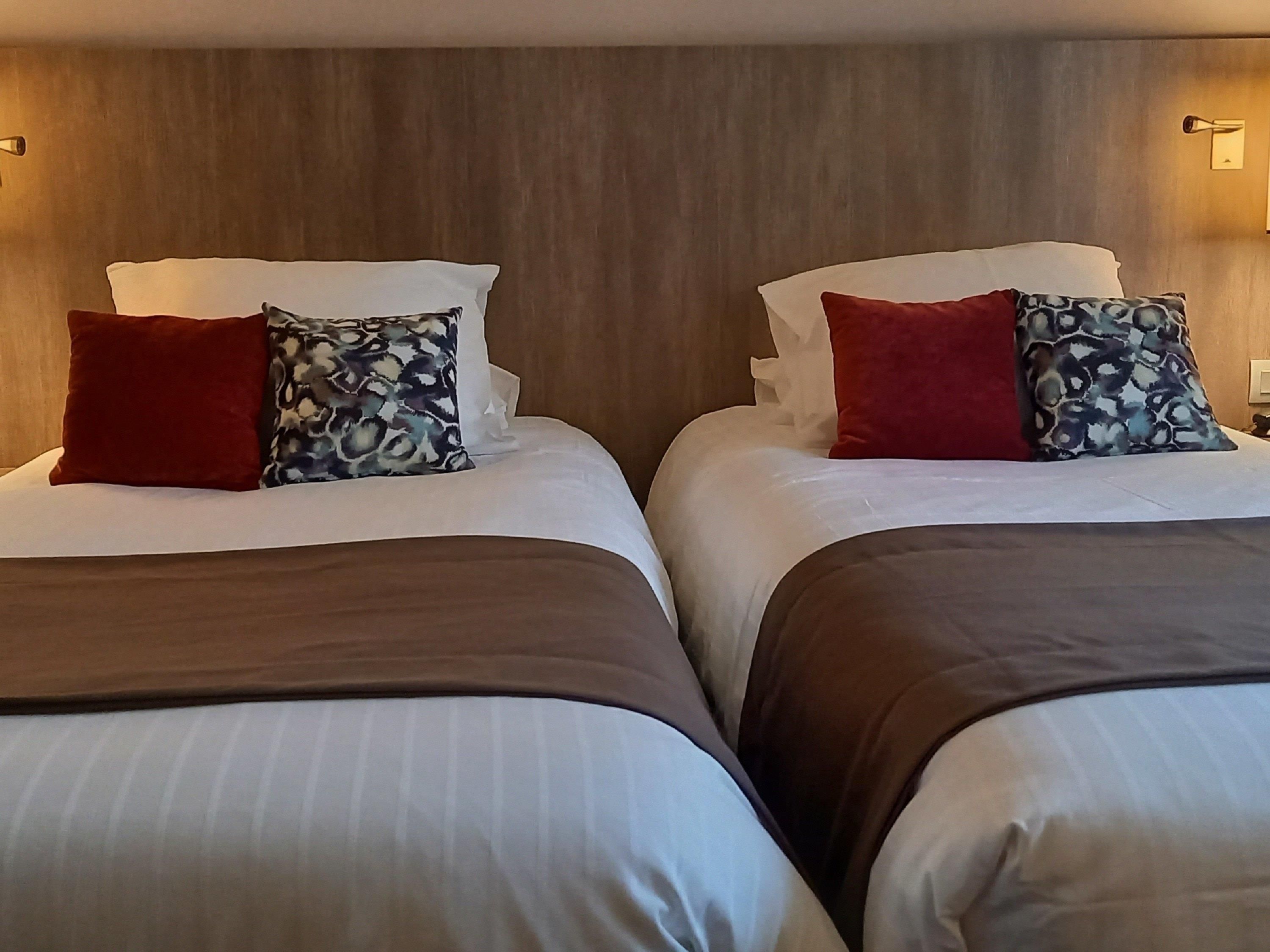 Two adjacent beds with white linens, red and patterned pillows, and a wooden headboard.