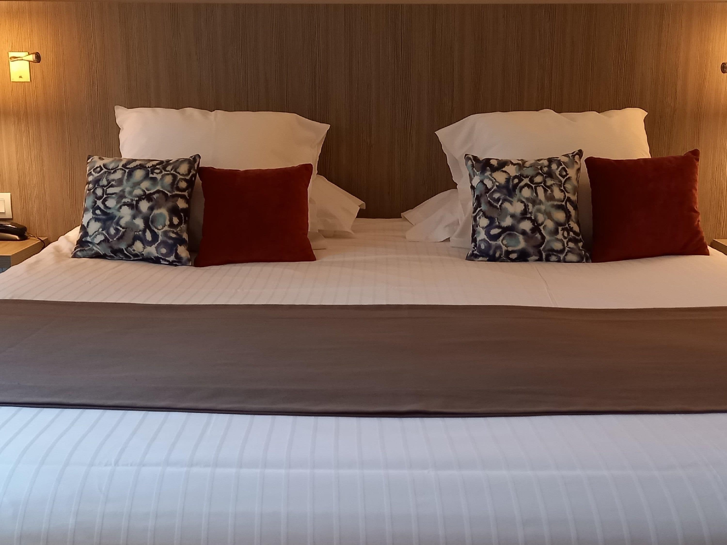A hotel room with a wooden headboard, two beds with white linens, and patterned pillows.