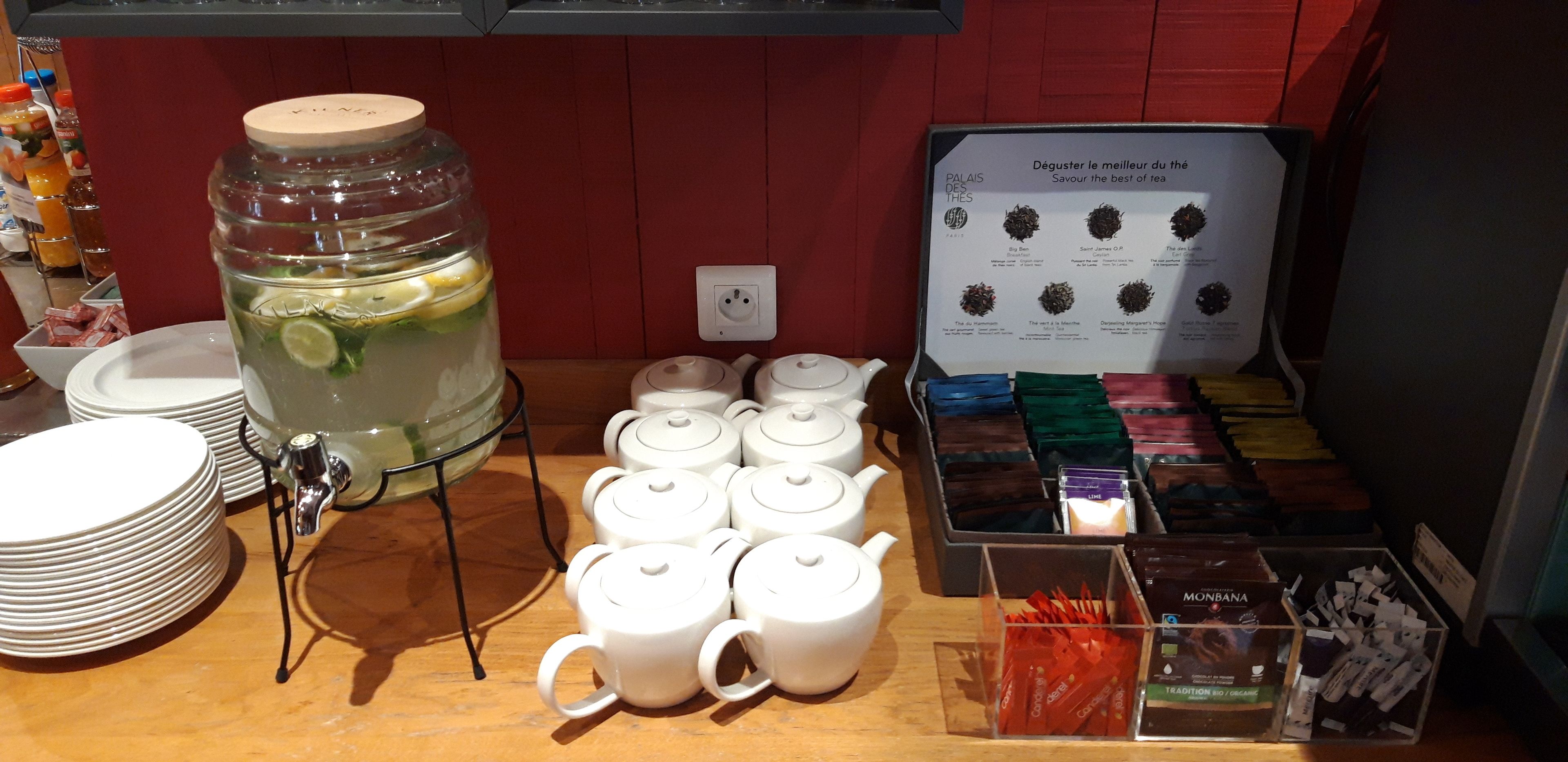 A tea station with a large pitcher, multiple teapots, and a tea selection board.
