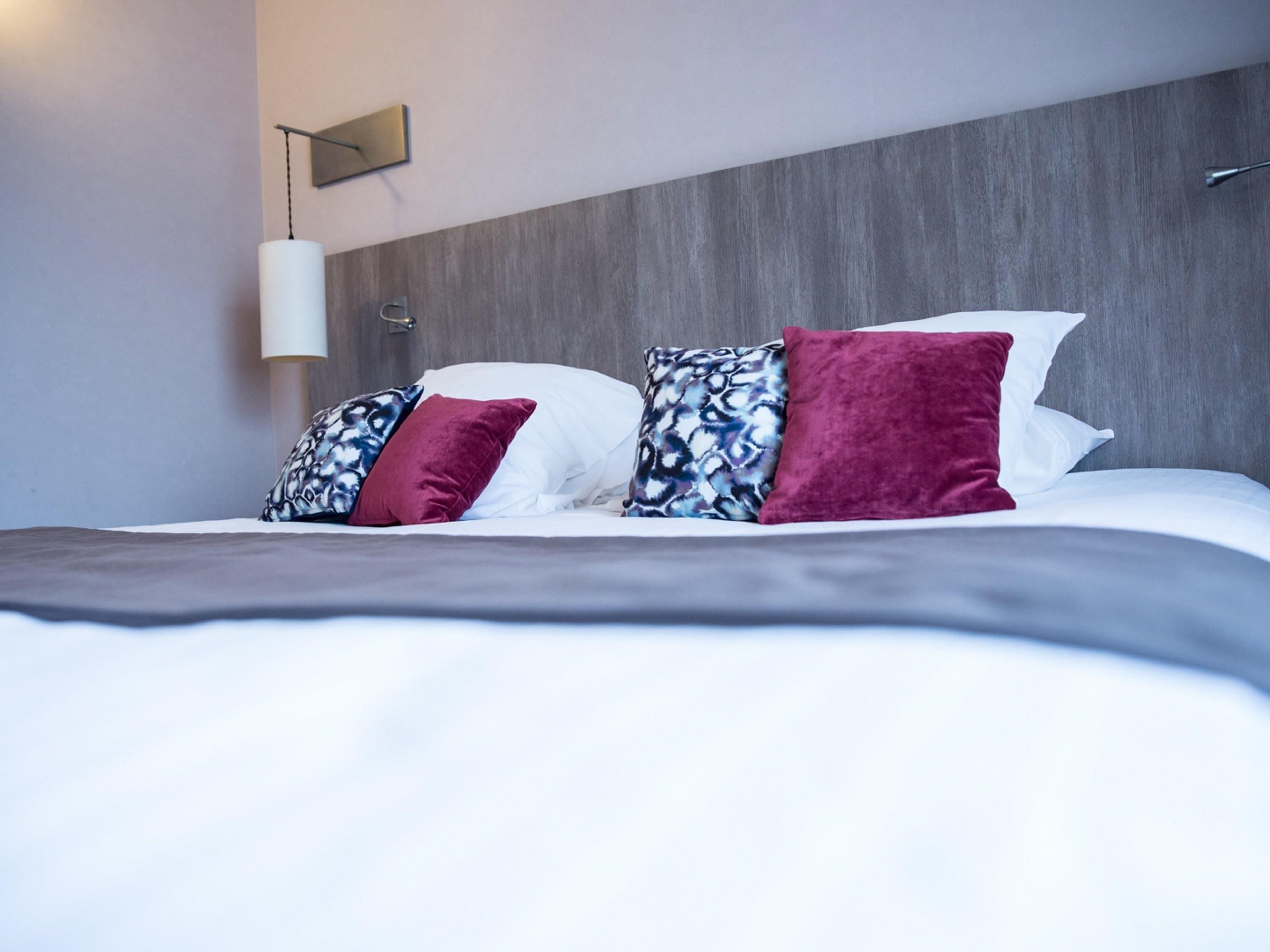 Quarto de hotel moderno com uma cama grande, luminária de cabeceira e cabeceira de madeira.