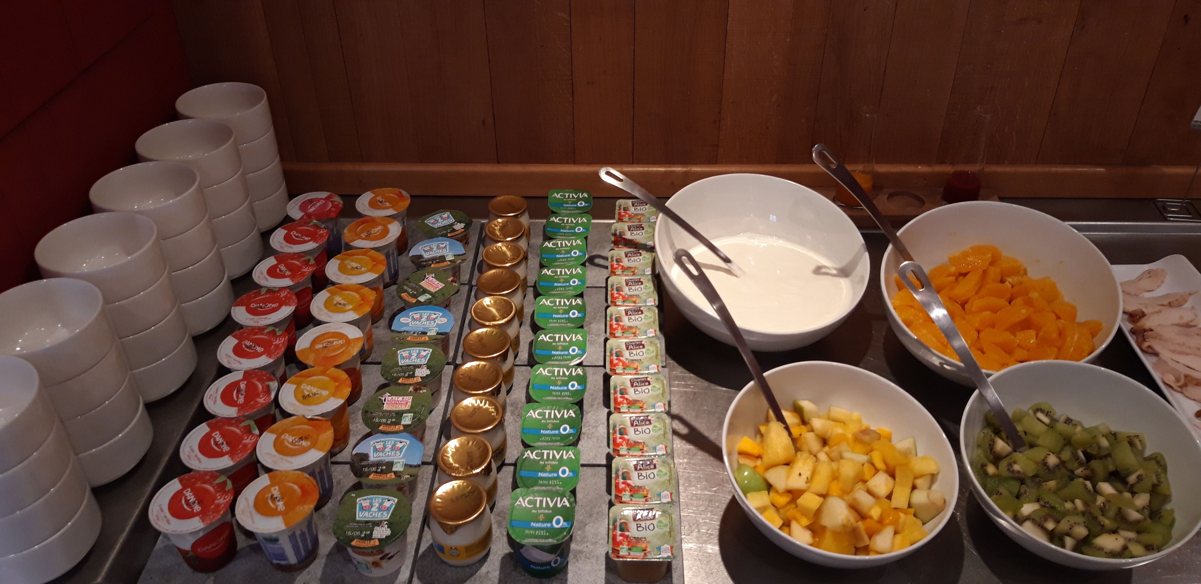 Une table de buffet garnie de divers aliments et de différents récipients, notamment des saladiers remplis de fruits et des piles de tasses.