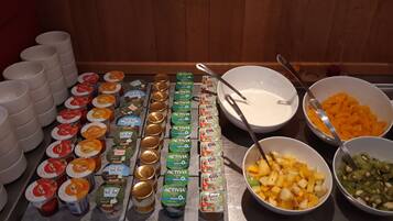 Une table de buffet garnie de divers aliments et de différents récipients, notamment des saladiers remplis de fruits et des piles de tasses.