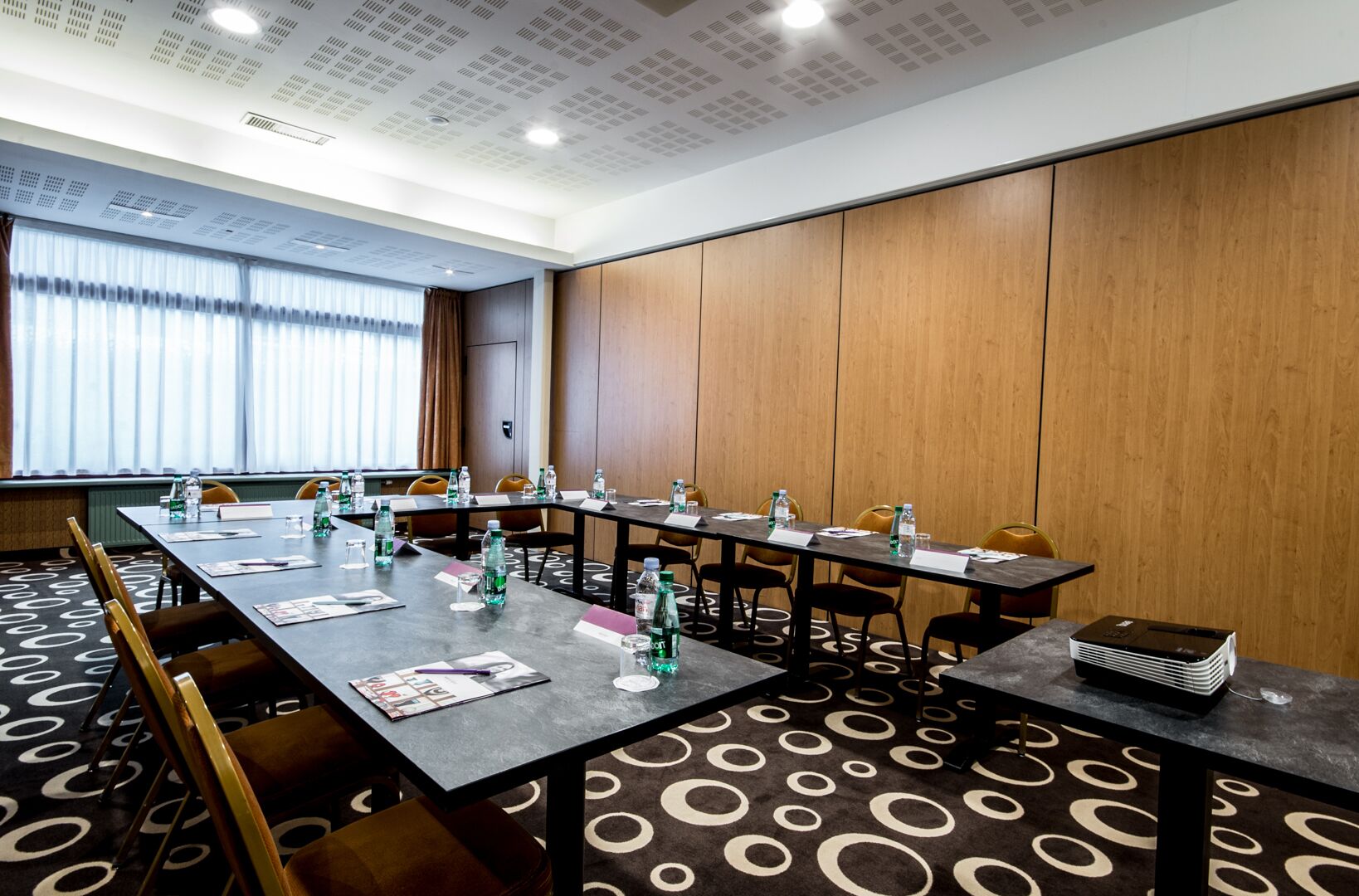 A conference room with long tables, chairs, water bottles, papers, and a projector.