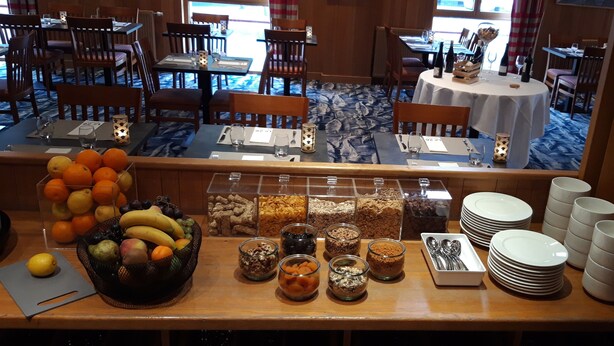 Un buffet de petit-déjeuner avec des fruits, des céréales et des assiettes blanches.