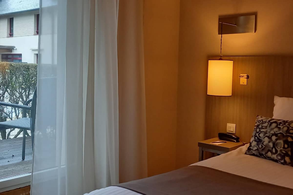 Ein Hotelzimmer mit Bett, Nachttisch mit Telefon, Lampe und Blick ins Freie.