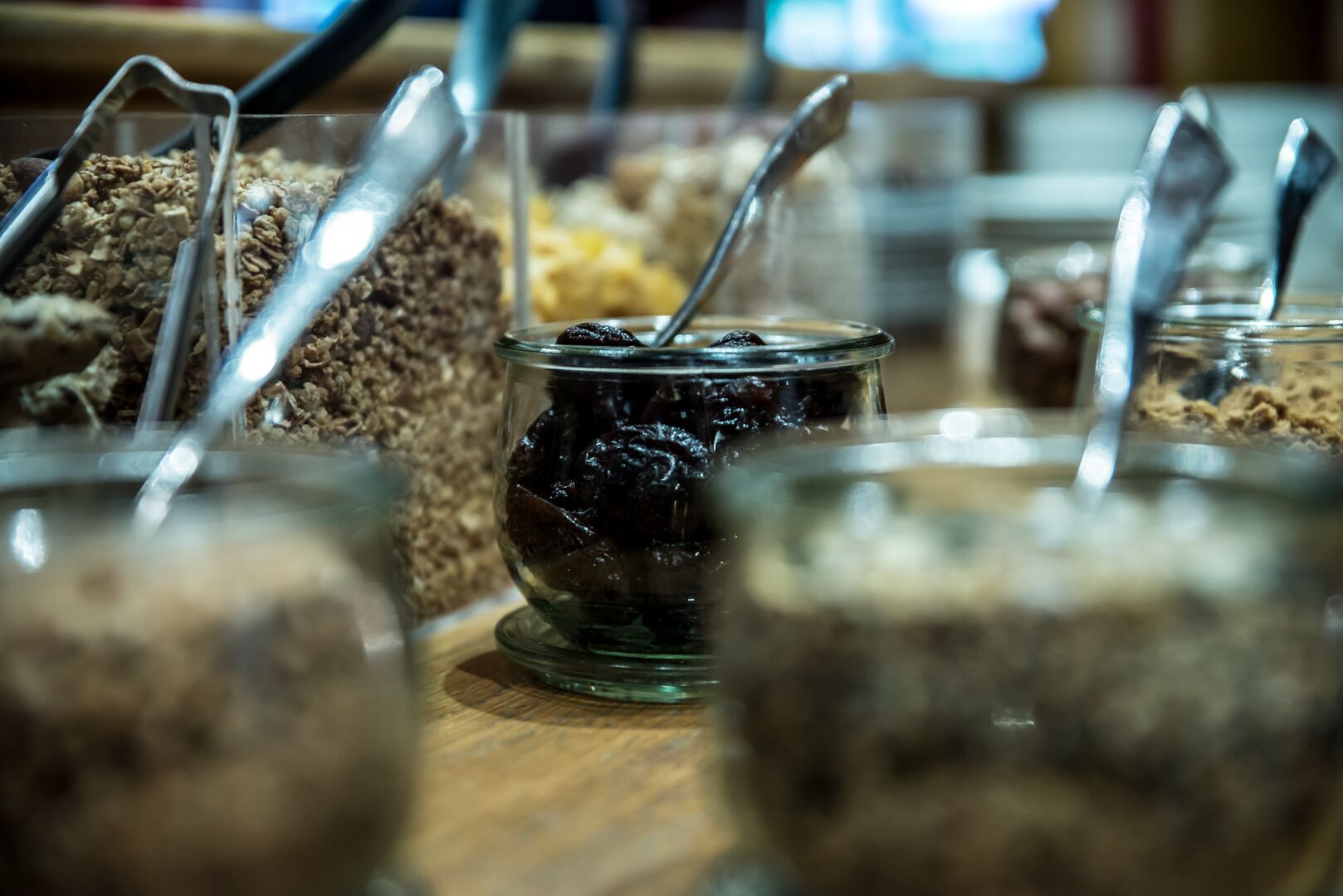 A variety of food items in glass containers with spoons, likely in a buffet setting.
