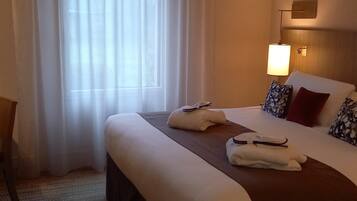 A hotel room with a large bed, a nightstand, a lamp, and sheer curtains.