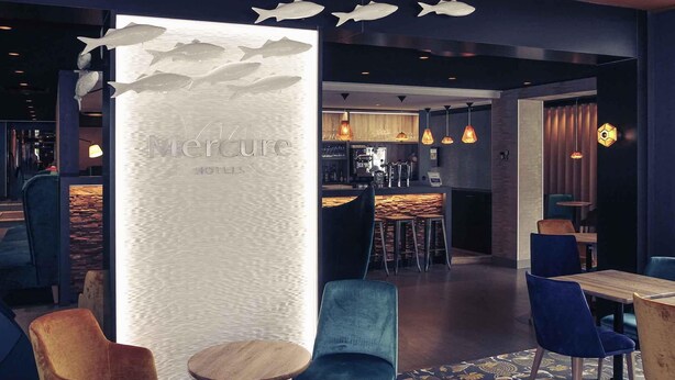 A modern interior with a bar area, seating with blue and wooden chairs, and a decorative wall with fish motifs. - Mercure Dinan Port Le Jerzual (Lanvallay)