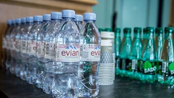 Des rangées de bouteilles d’eau Evian et de bouteilles de soda Bado sont alignées sur une table.