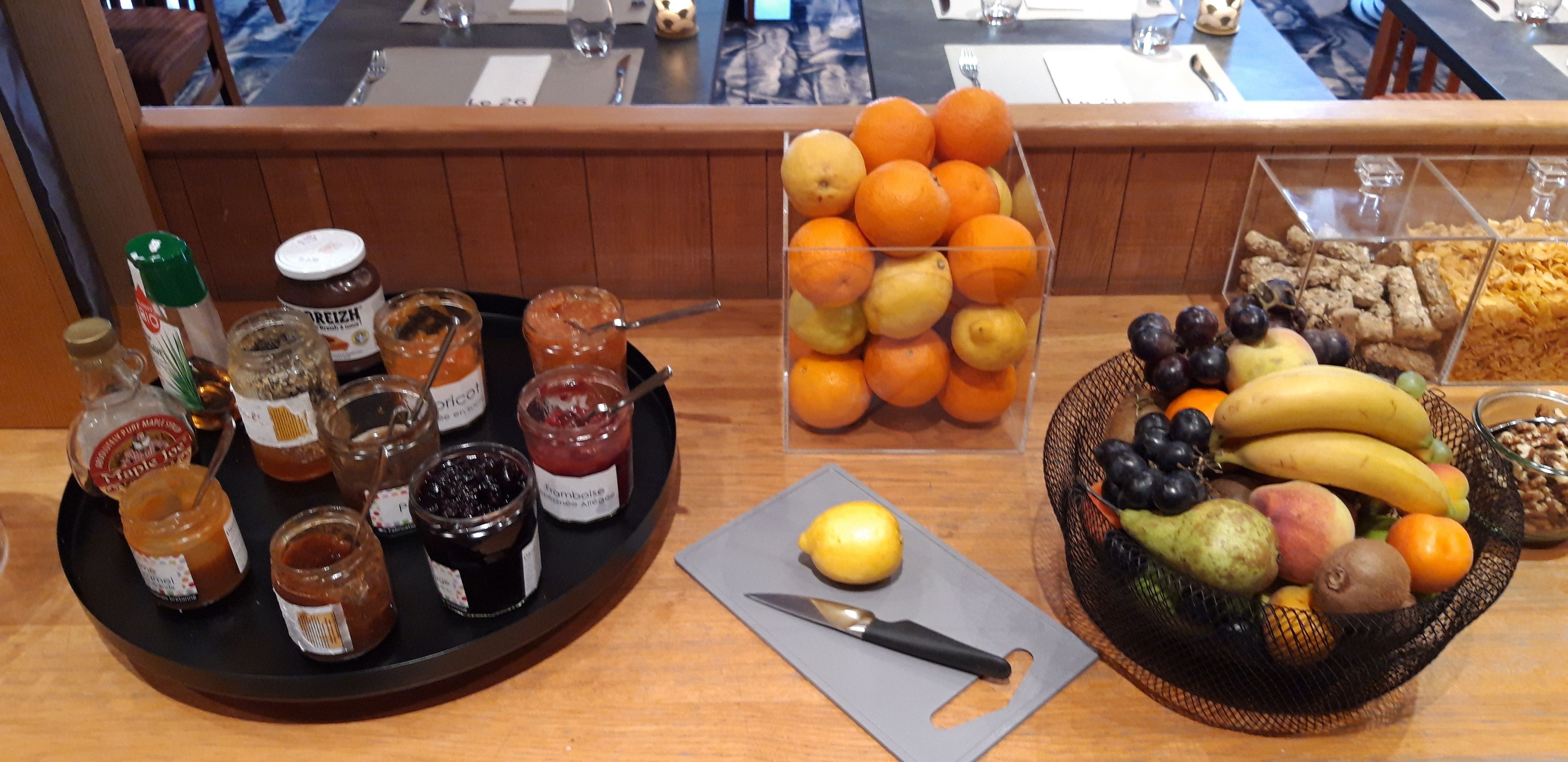 A breakfast spread with various jams, oranges, and a fruit basket.